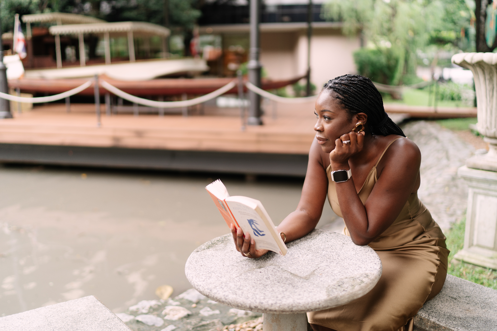 Issa reading by the water, wearing a gold silk dress